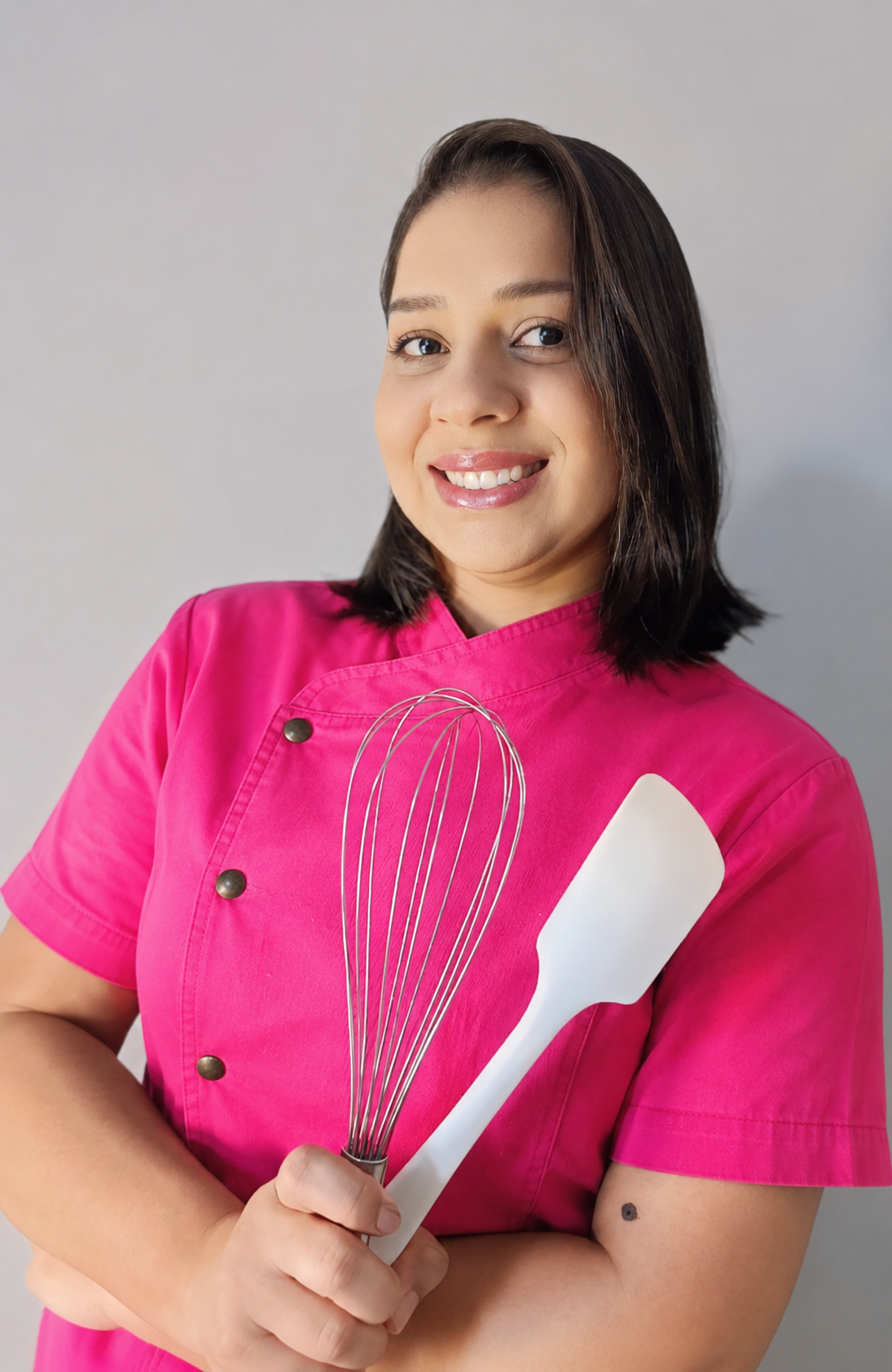 Suzi com uniforme rosa, segurando um batedor e uma espátula.
